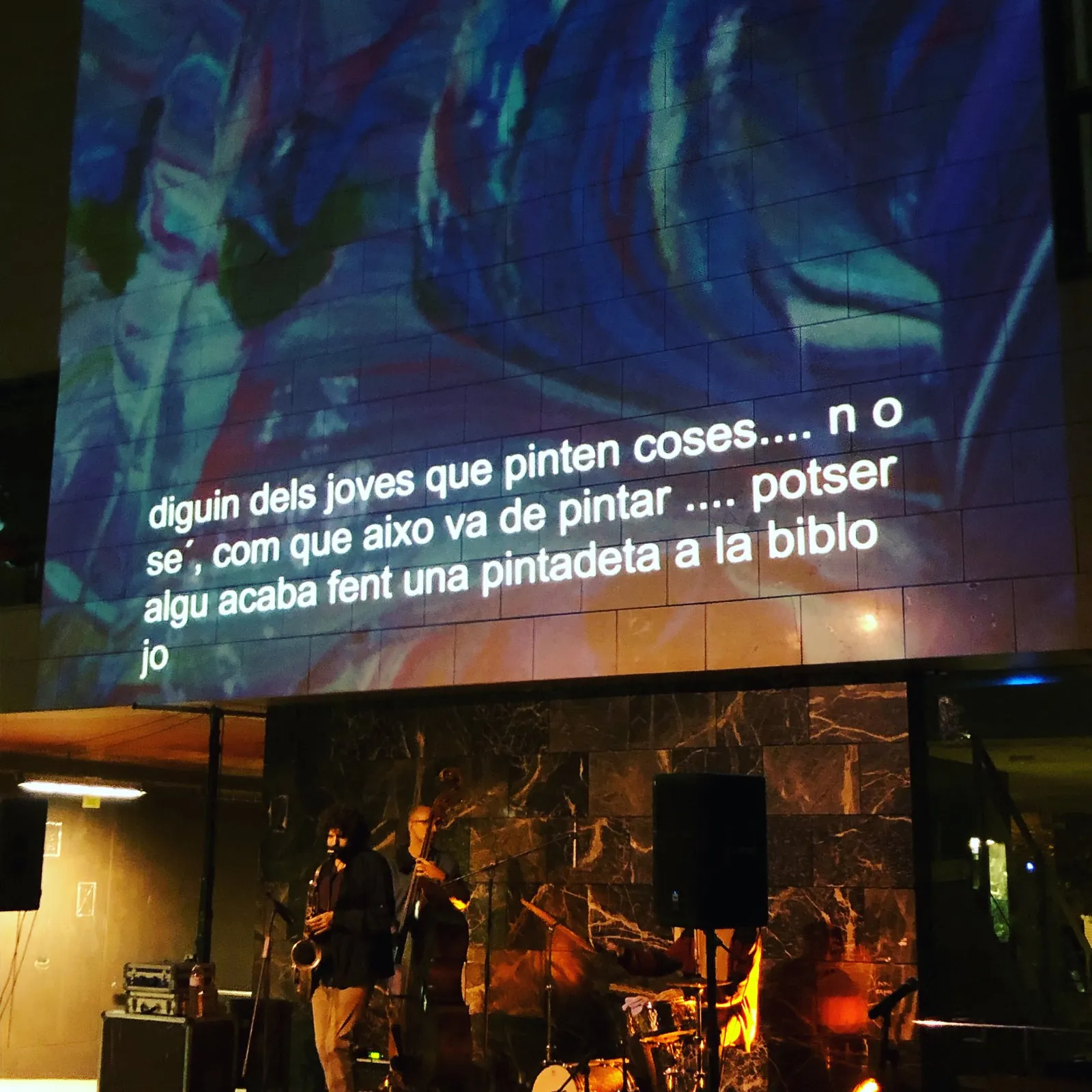 Text projected onto a wall with live musicians below